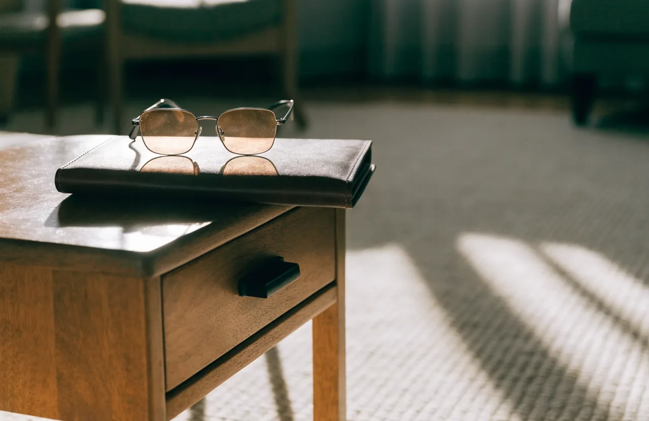Mesa de madera bajo una lámpara cálida con carpeta en blanco, lápiz y gafas de lectura